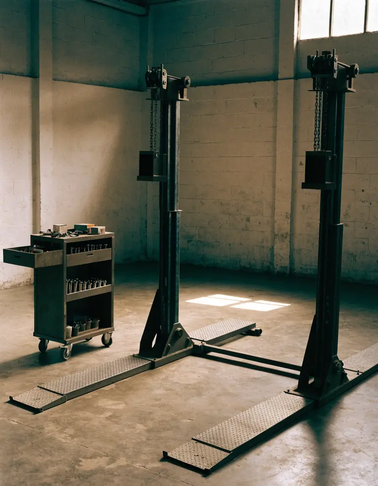 An empty service bay with a lowered two-post lift and a tool trolley, daylight falling across the floor.